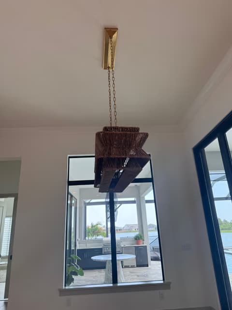 Gold branch-style pendant chandelier hanging in a two-story foyer with tall windows