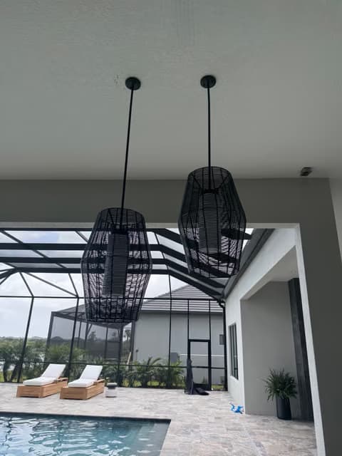 Black pendant lights installed over a screened pool lanai under construction