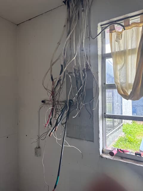 Open wall with exposed electrical wiring bundle near a window during a renovation