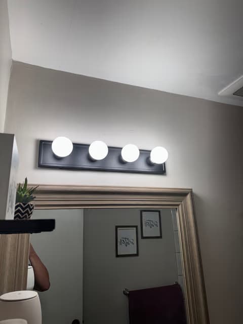 Wall-mounted bathroom vanity light with four round bulbs above a mirror