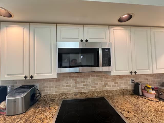 White kitchen cabinets with a new stainless steel microwave and tile backsplash