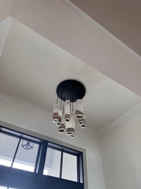 Round chandelier fixture installed near a black-framed window under a high ceiling