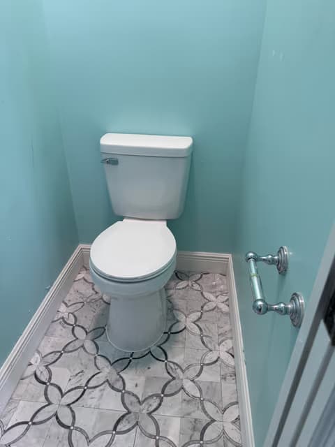 Small bathroom with a new toilet, patterned tile floor, and teal walls
