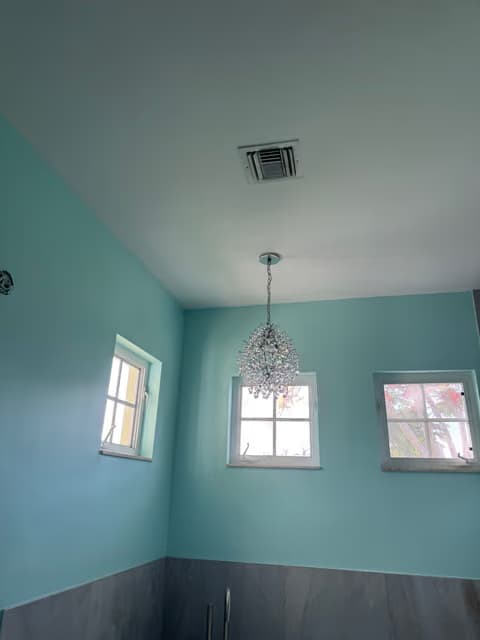Teal-walled dining nook with a chandelier and large windows
