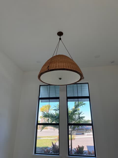 Woven pendant light fixture installed in a tall foyer with windows